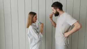 A couple brushing their teeth indoors, sharing a morning routine. Side view highlights interaction.
